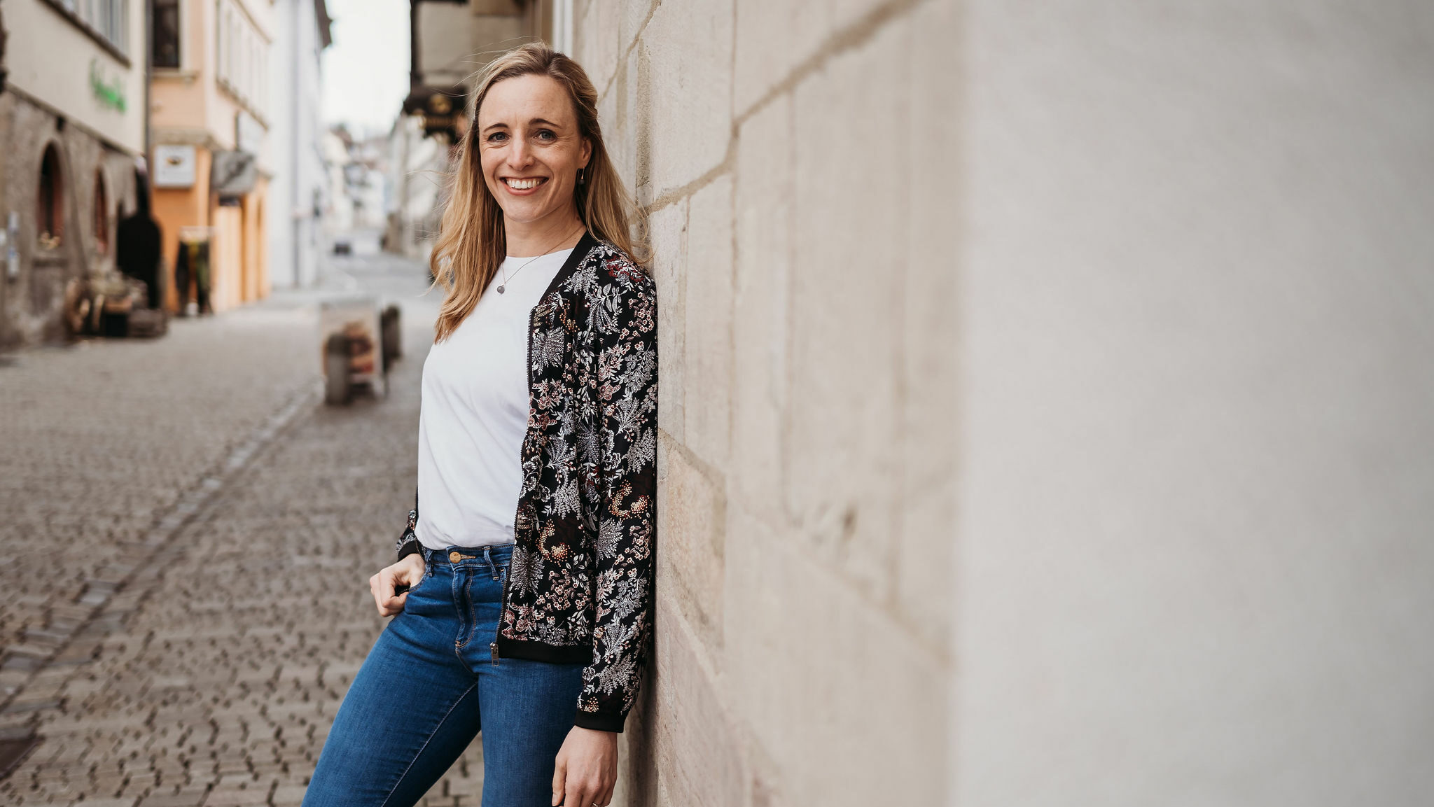 Blonde Frau lehnt an einer Steinwand und lächelt in die Kamera Mette_Vasterling_Businessfotografie_Braunschweig