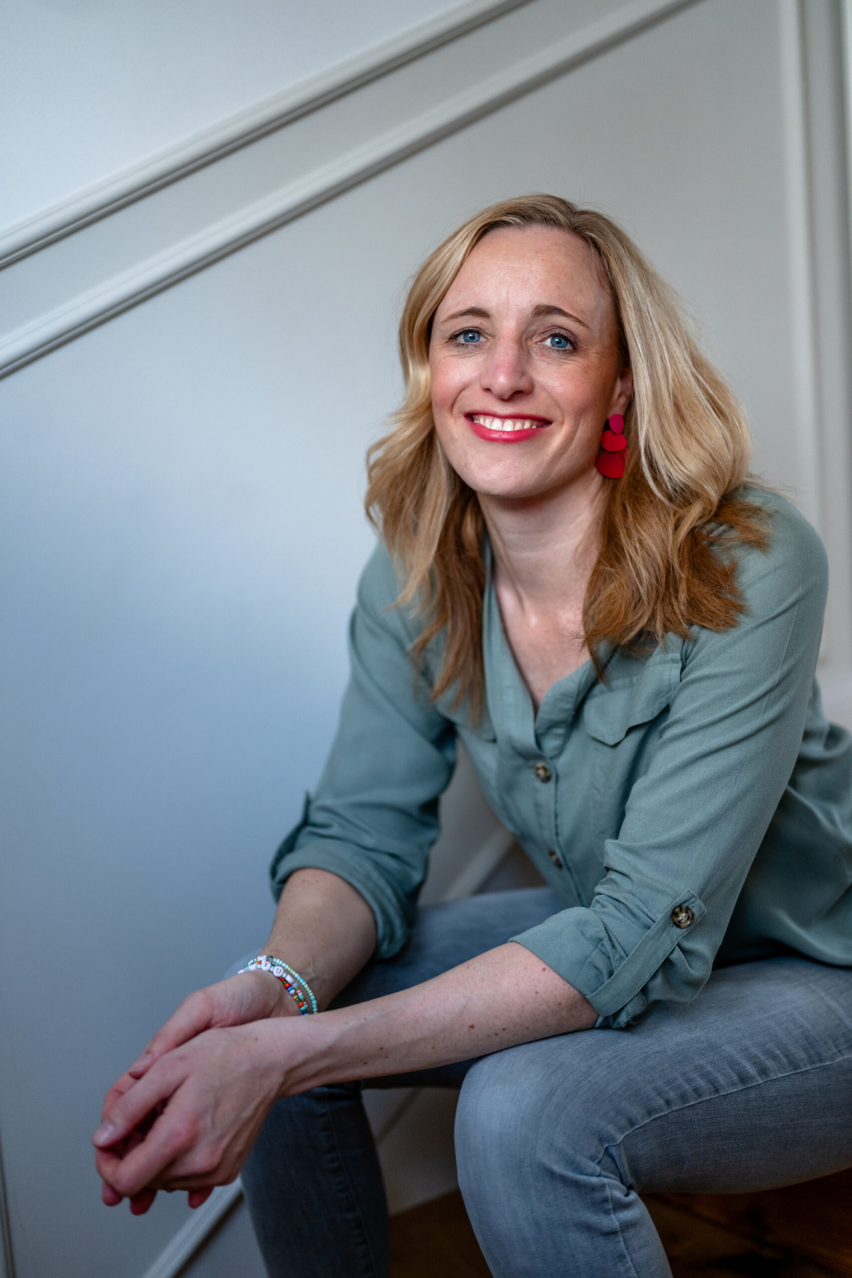 Blonde Personal Branding Fotografin sitzt auf einer Treppe und schaut lächelnd in die Kamera.